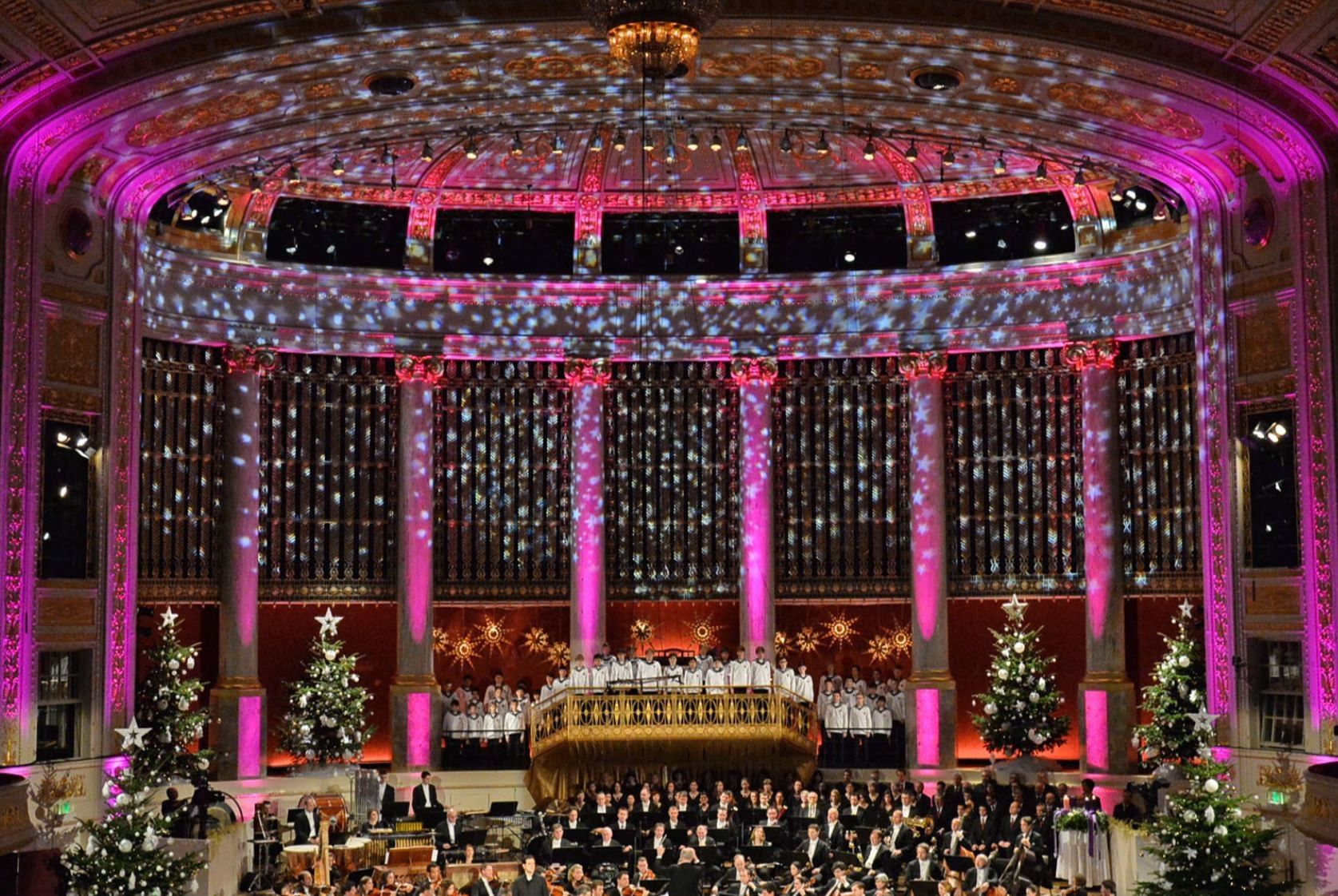 Festively decorated concert hall at the Vienna Konzerthaus with Christmas lights, trees, choir, and orchestra on stage.