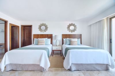 Resort bedroom with two beds looking out through large glass windows towards a private terrace.