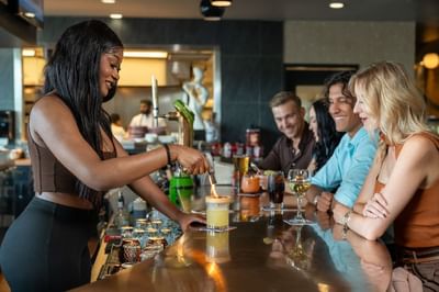 A woman pours the drink into a glass on bar counter at Hotel Clique Calgary Airport