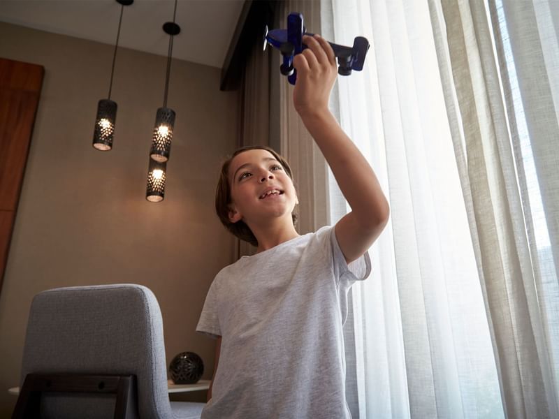 A kid holding up a toy airplane indoors at Fiesta Americana