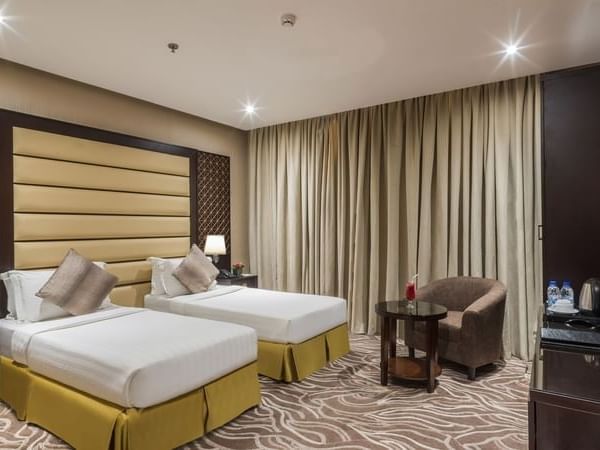 Twin beds by a round table with a drink under a long tan curtain in Deluxe King / Twin Room at Naviti by Warwick Al Khobar