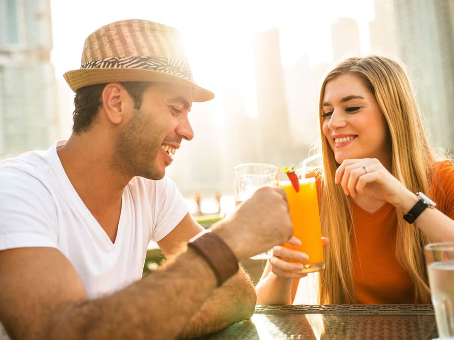 Two people sharing a toast with drinks at an outdoor table in a sunny setting near DAMAC Hotels & Resorts