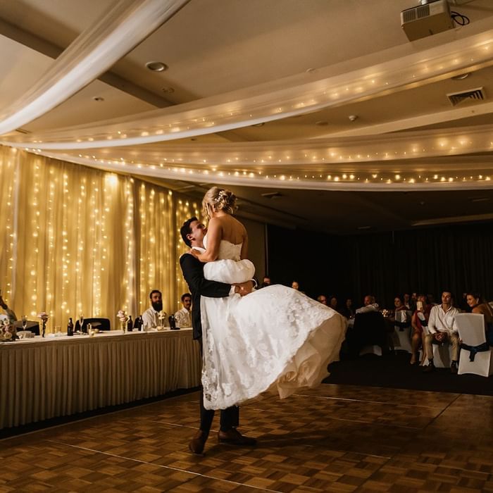 Groom lifting a bride in a dance with fairy lights backdrop at Mercure Kooindah Waters