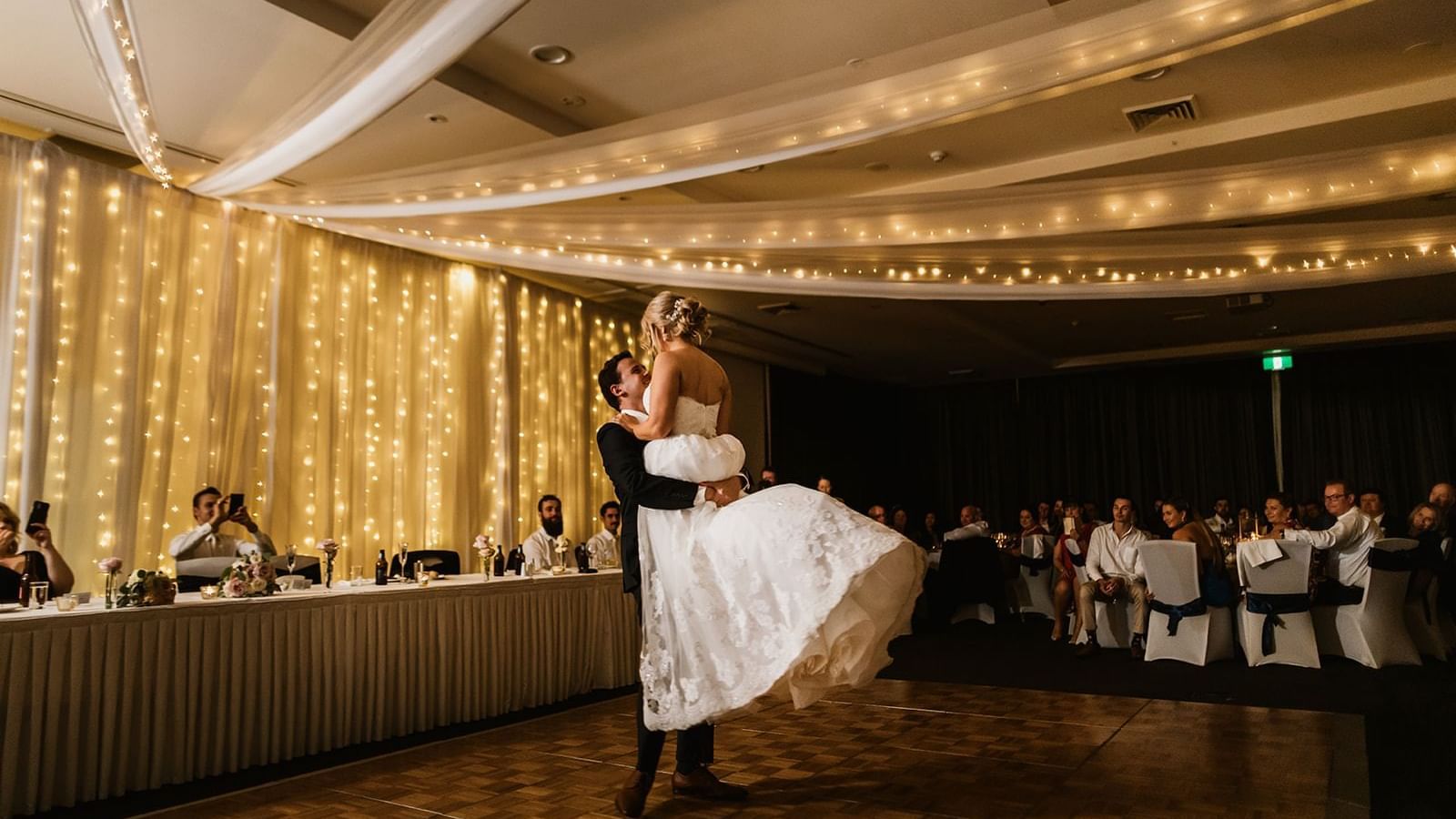 Groom lifting a bride in a dance with fairy lights backdrop at Mercure Kooindah Waters