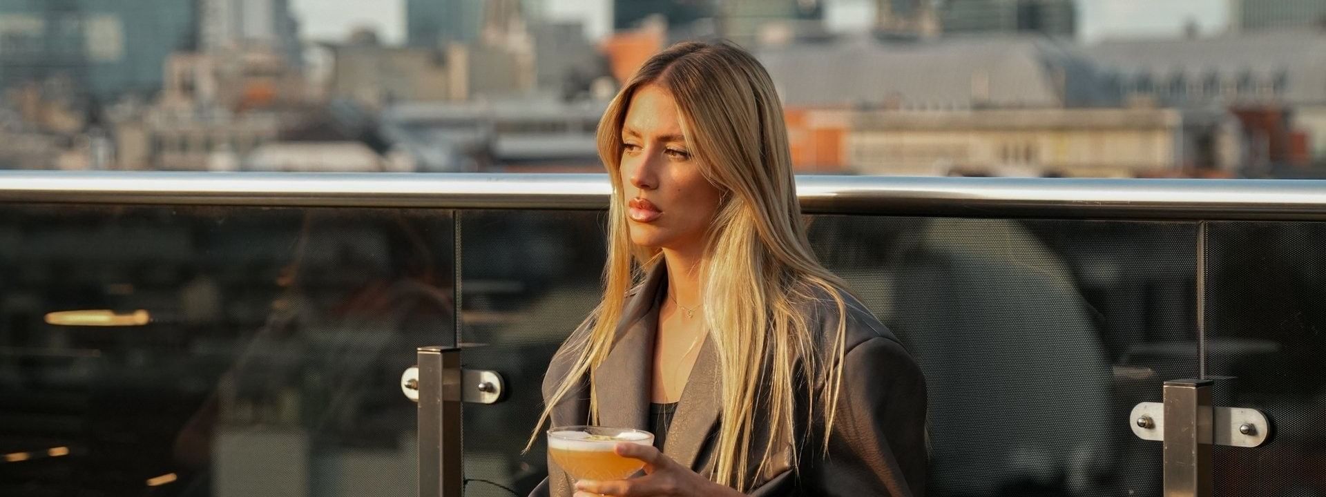 Vrouw met cocktail op het dakterras met uitzicht op de stad bij Secret Rooftop by Warwick in Brussel.