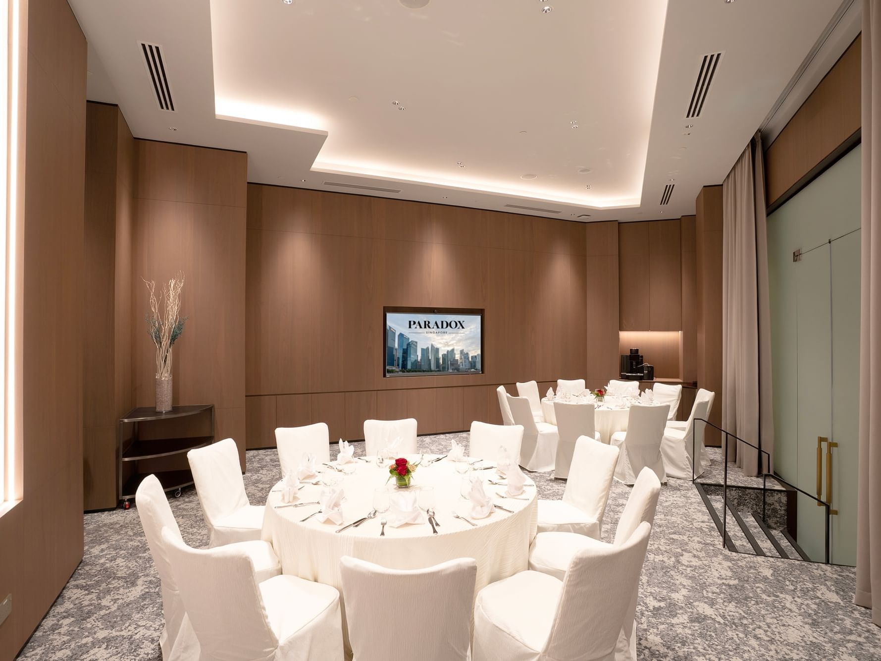 Round table banquet setting at Paradox Singapore, featuring elegantly dressed tables with white linens, neatly arranged place settings, glassware, and floral centerpieces in a well-lit meeting room.