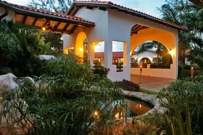 Lit torches and warm lights illuminating an open archway entrance with lush greenery at Sugar Cane Club Hotel & Spa