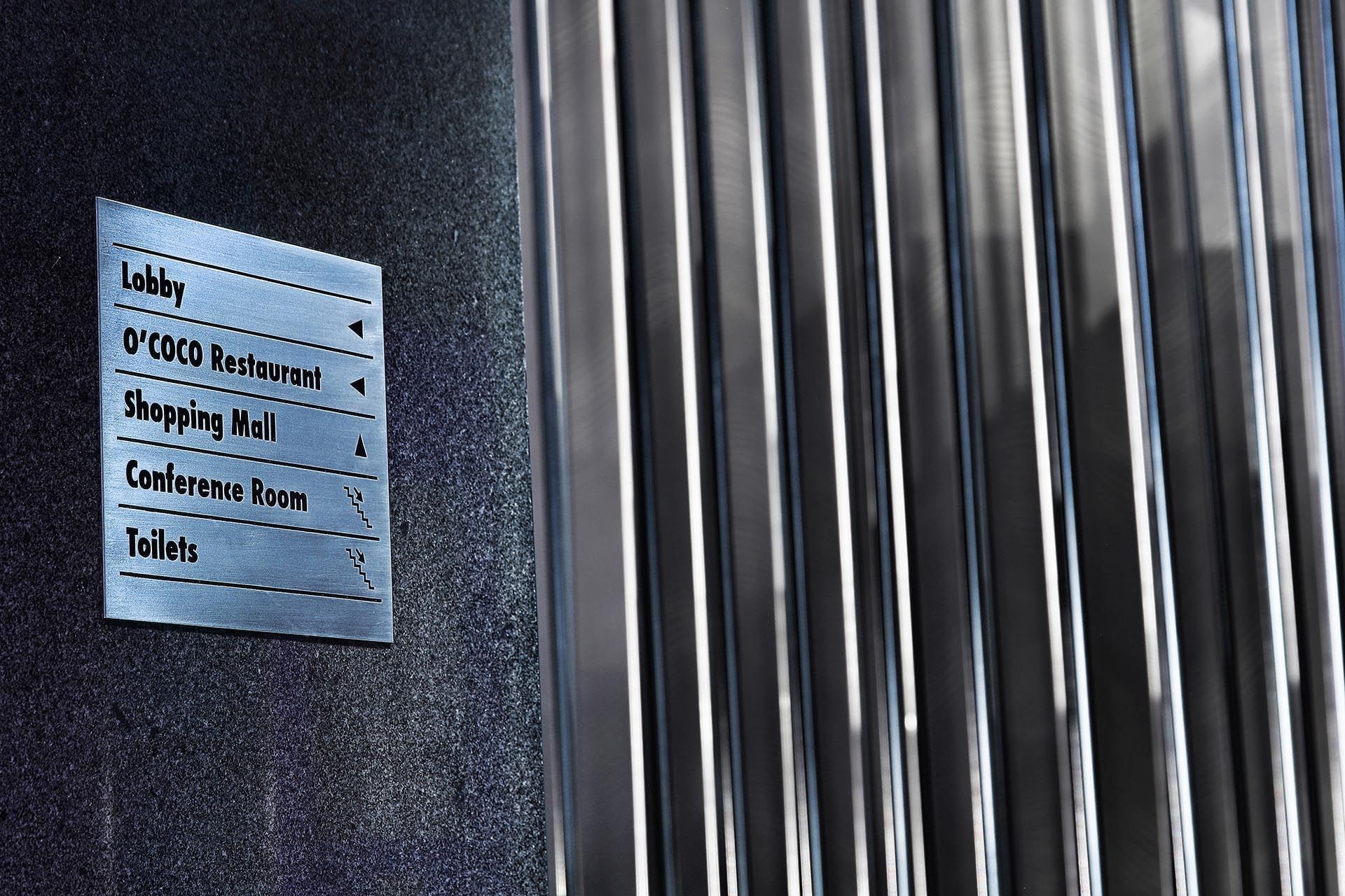 Metal directory sign by a fluted wall near the elevators and lobby area at Warwick Stone 55 - Beirut