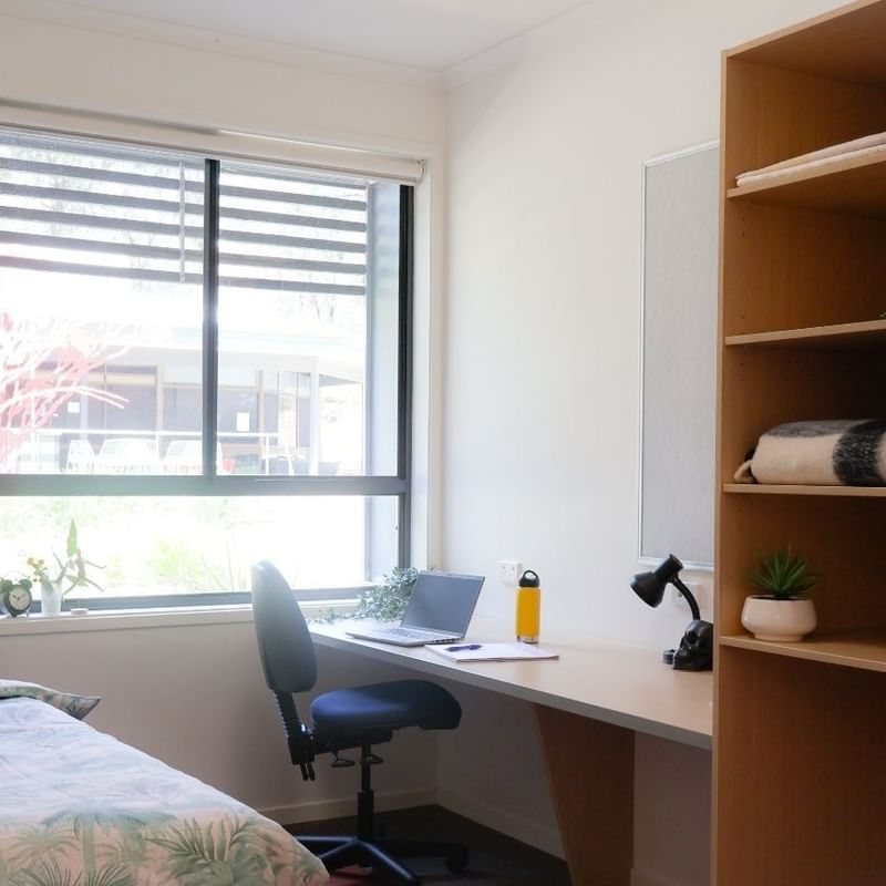Cozy bedroom with a bed, desk, chair, bookshelf, and window at Hillside Apartments.