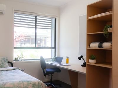 Cozy bedroom with a bed, desk, chair, bookshelf, and window at Hillside Apartments.