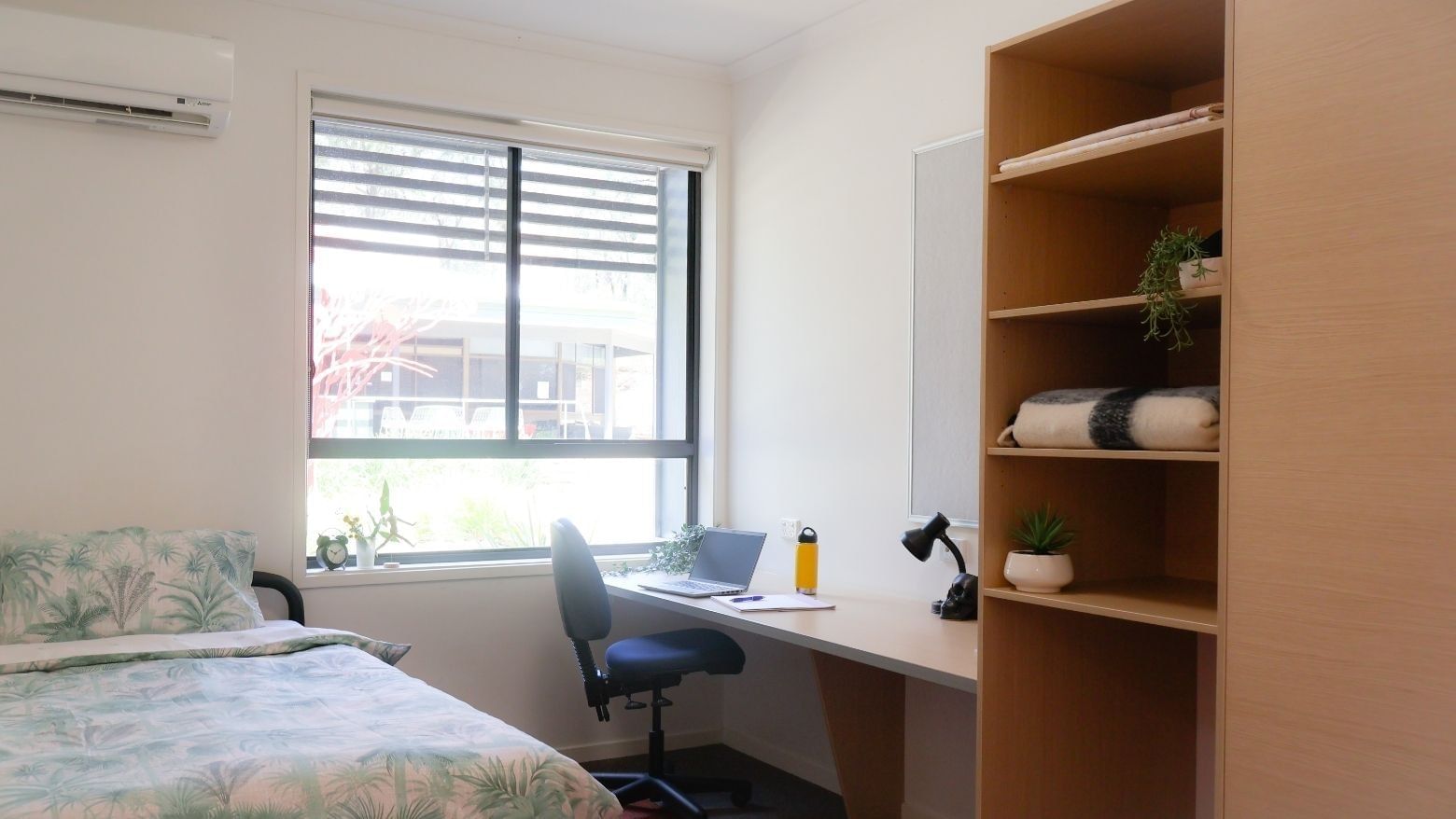 Cozy bedroom with a bed, desk, chair, bookshelf, and window at Hillside Apartments.