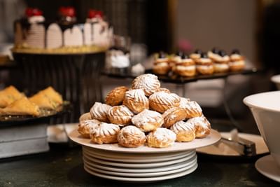 Large stack of cream puffs dusted with powdered sugar on a dessert buffet table at Saja Warwick Madinah