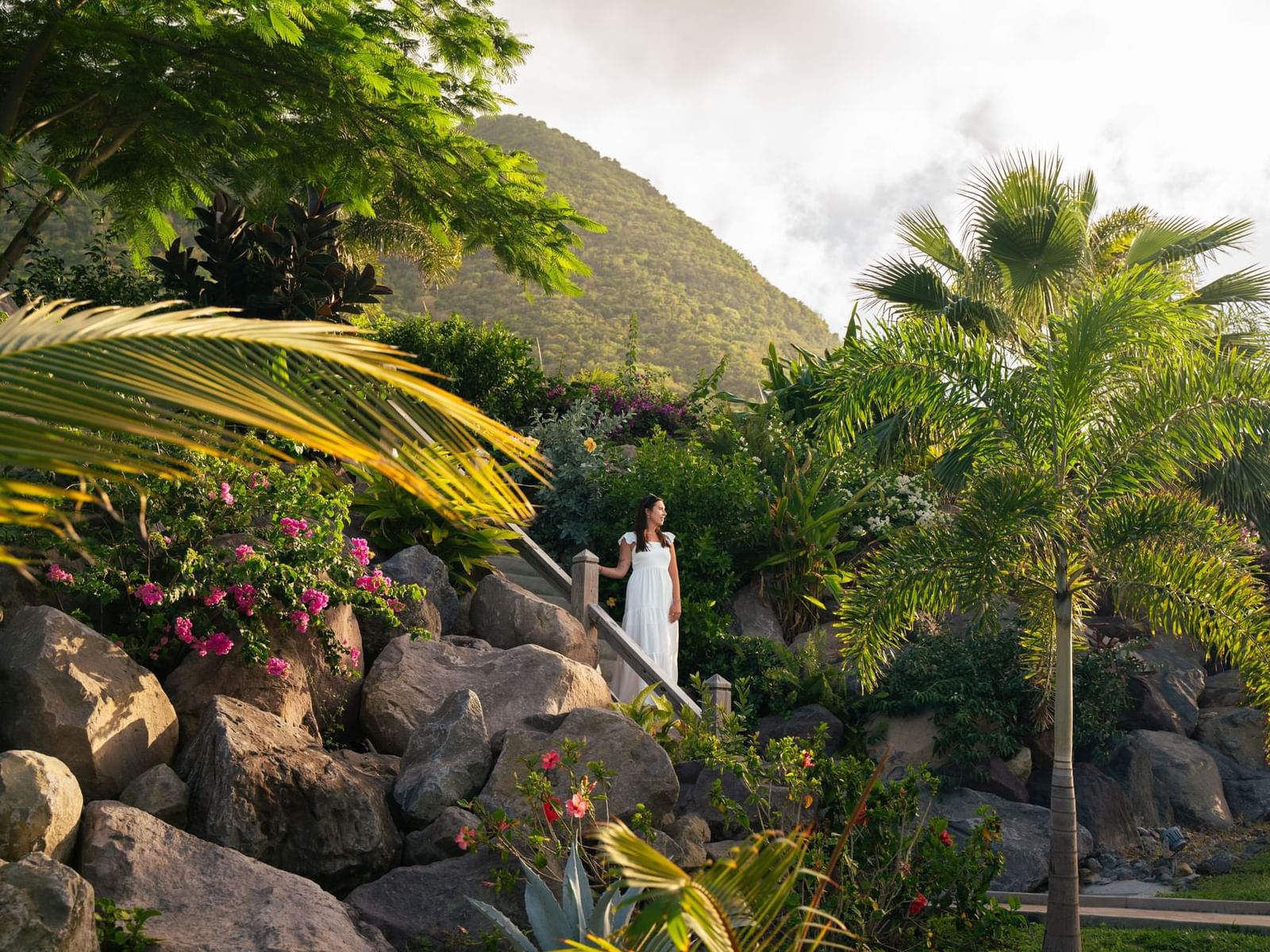 Woman on stone path amid greenery and flowers with mountain backdrop at Golden Rock Resort