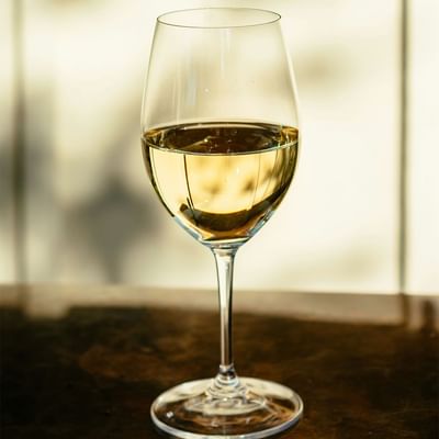Clear wine glass with white wine on a table, set against a blurred background.