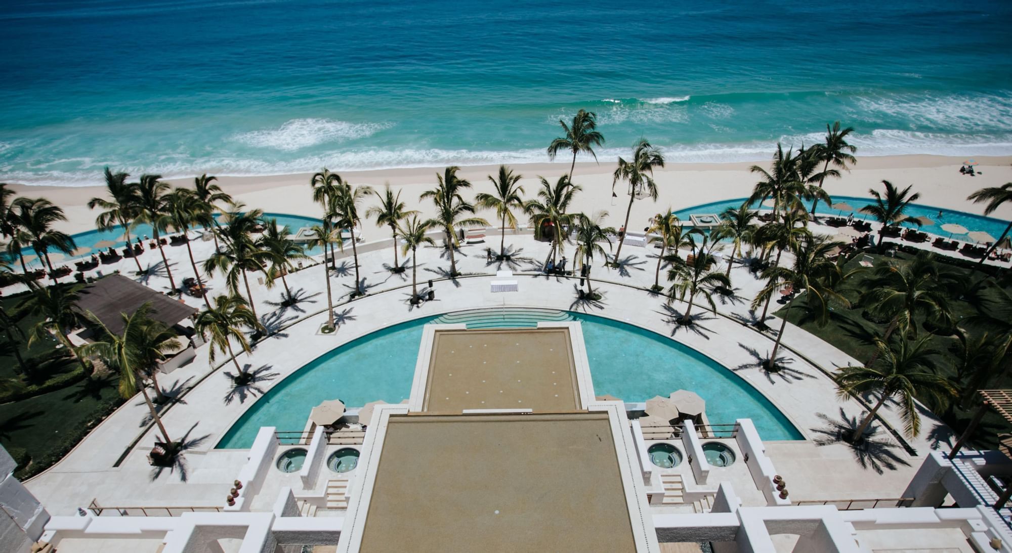 Aerial view of Marquis Los Cabos Resort with sparkling pools and palm trees along a pristine beach
