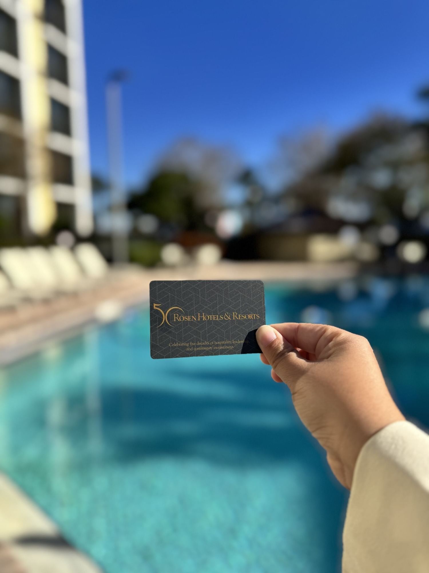 A hand holds a Rosen Hotels & Resorts key card in front of a bright blue pool.