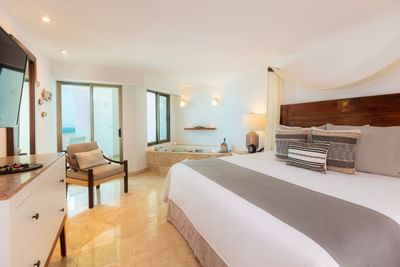 Hotel room with bed, chair, dresser, and balcony with ocean view.