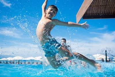 Young man jumping into sparkling blue pool with friends on sunny day at Playa Los Arcos Puerto Vallarta 2023