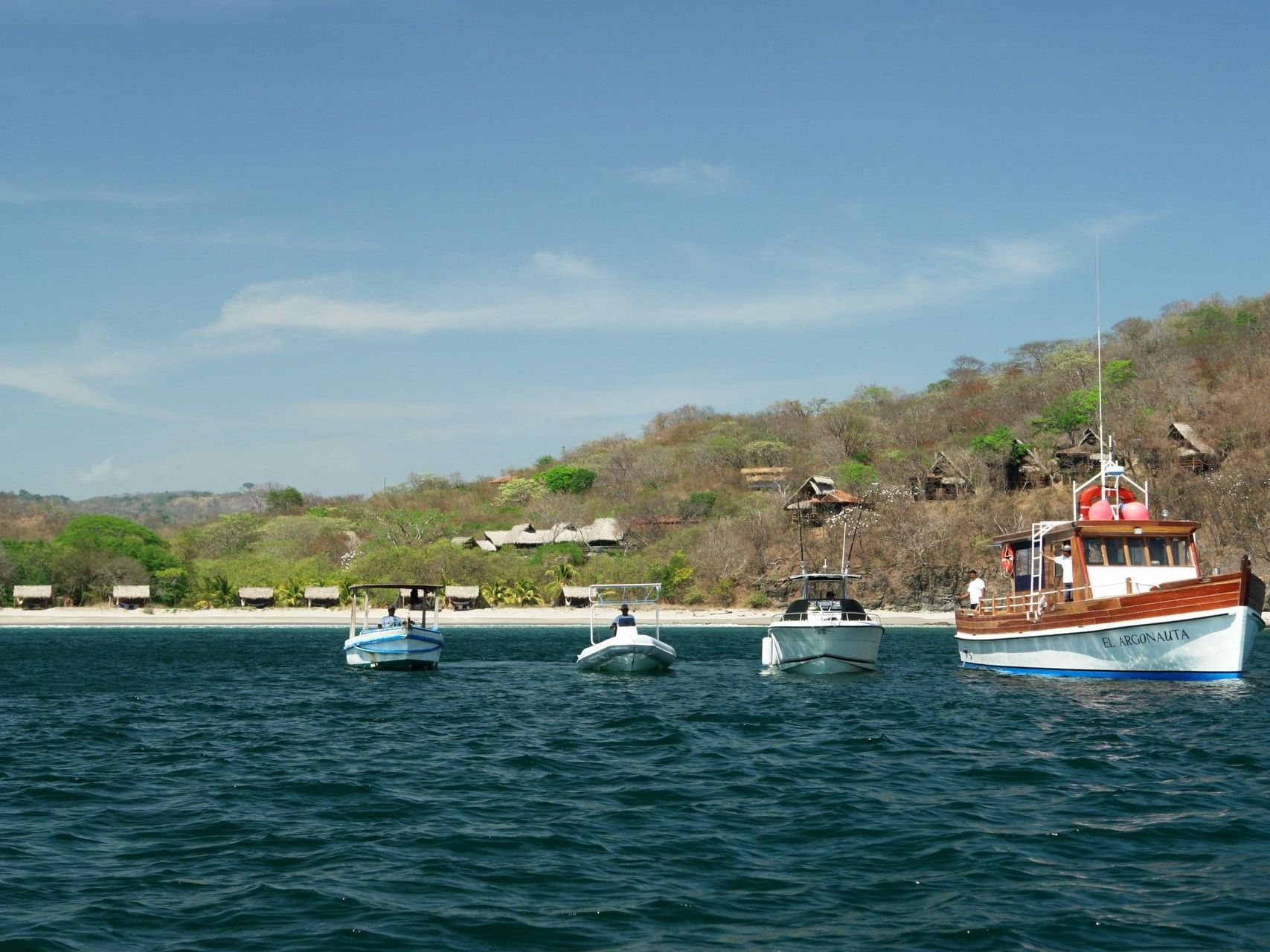 Four boats by a tropical shoreline under a clear sky near Morgan's Rock Reserve & Ecolodge