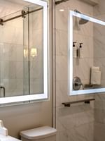 Marble walk-in shower by a glowing mirror under a warm wall sconce in Classic Double at Warwick Melrose Dallas