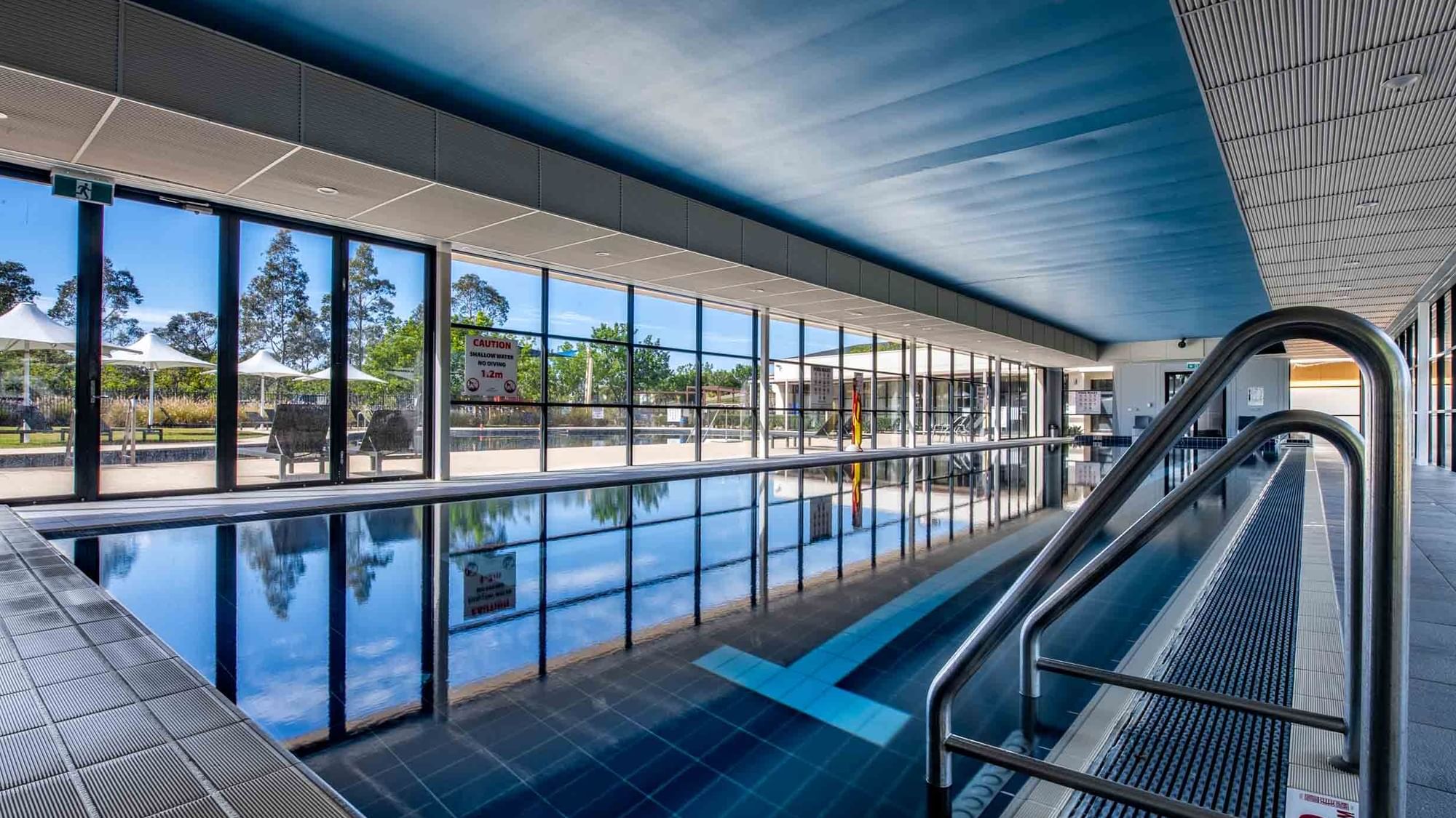 Indoor lap pool with reflective water, and large windows at Mercure Kooindah Waters