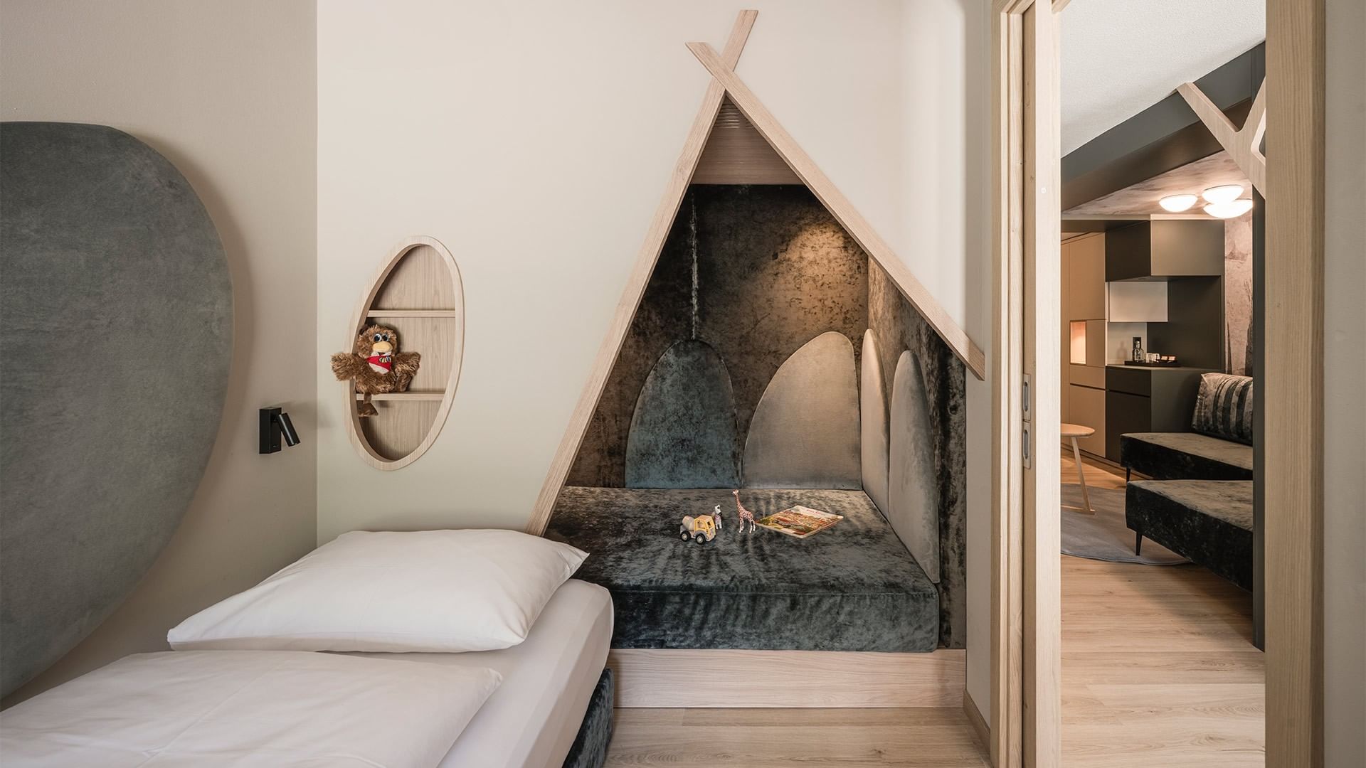 Camera da letto con letto singolo, tenda a forma di tenda e angolo gioco con peluche e libri.