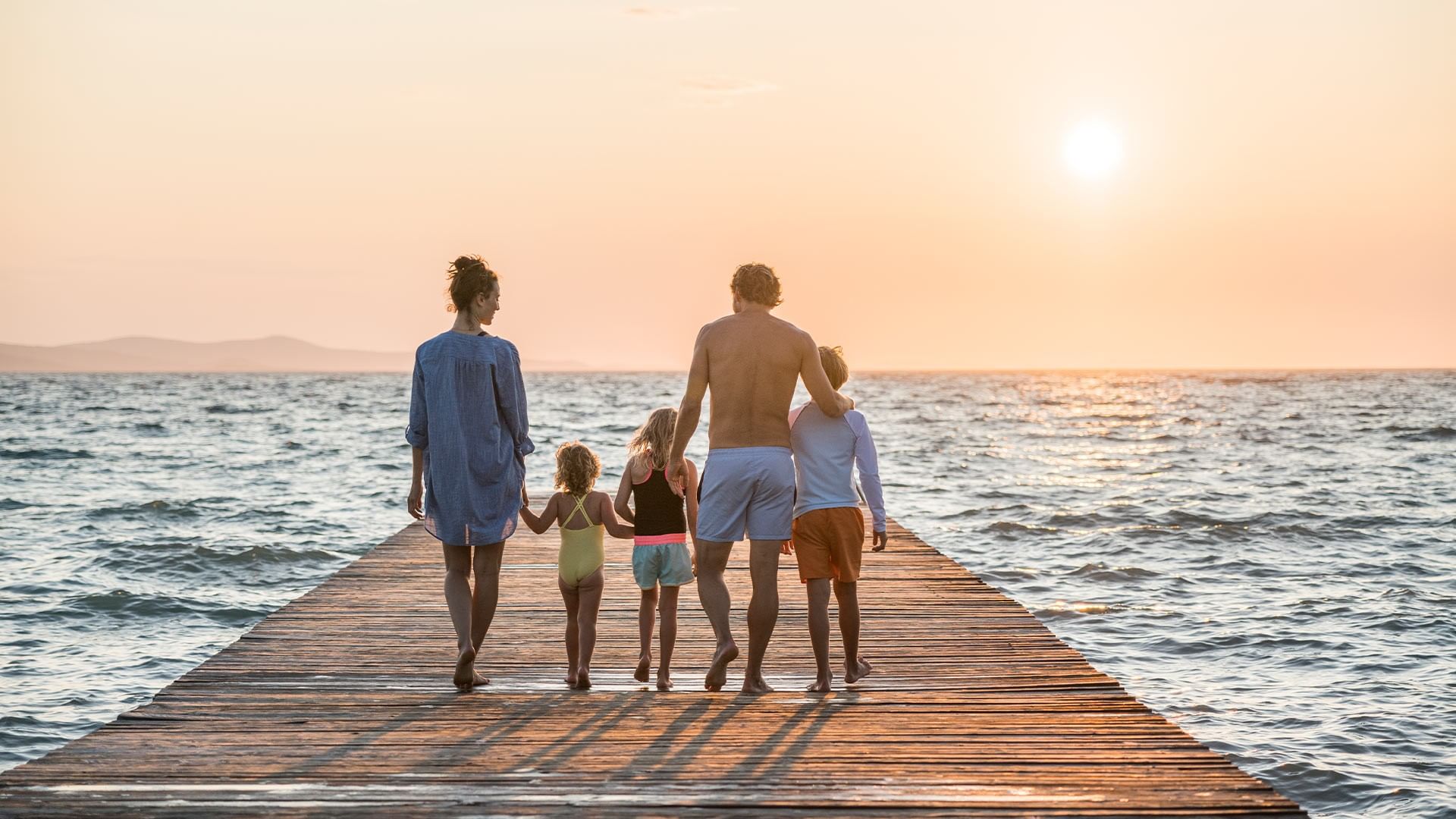 Family of four walking on a wooden pier at sunset at Falkensteiner Hotel & Spa Jesolo