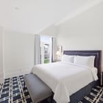 Bright guest room with white bedding, navy patterned carpet, and balcony doors at el PRADO Hotel