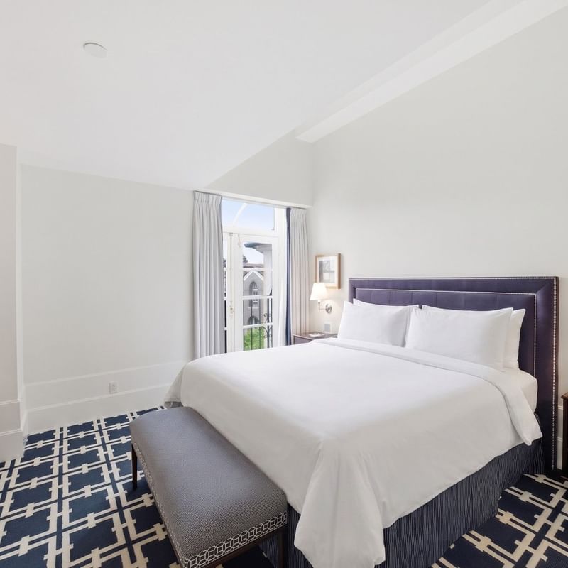 Bright guest room with white bedding, navy patterned carpet, and balcony doors at el PRADO Hotel
