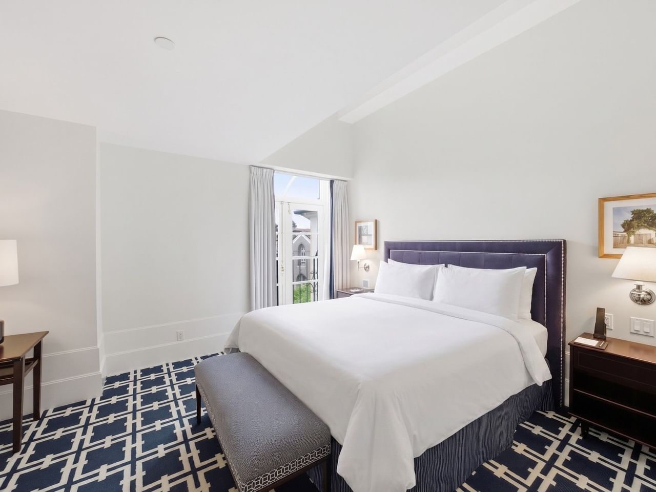 Bright guest room with white bedding, navy patterned carpet, and balcony doors at el PRADO Hotel