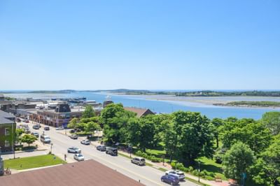 High-angle view of a coastal town street with cars, green trees, and a blue water bay beyond from Rodd Grand Yarmouth