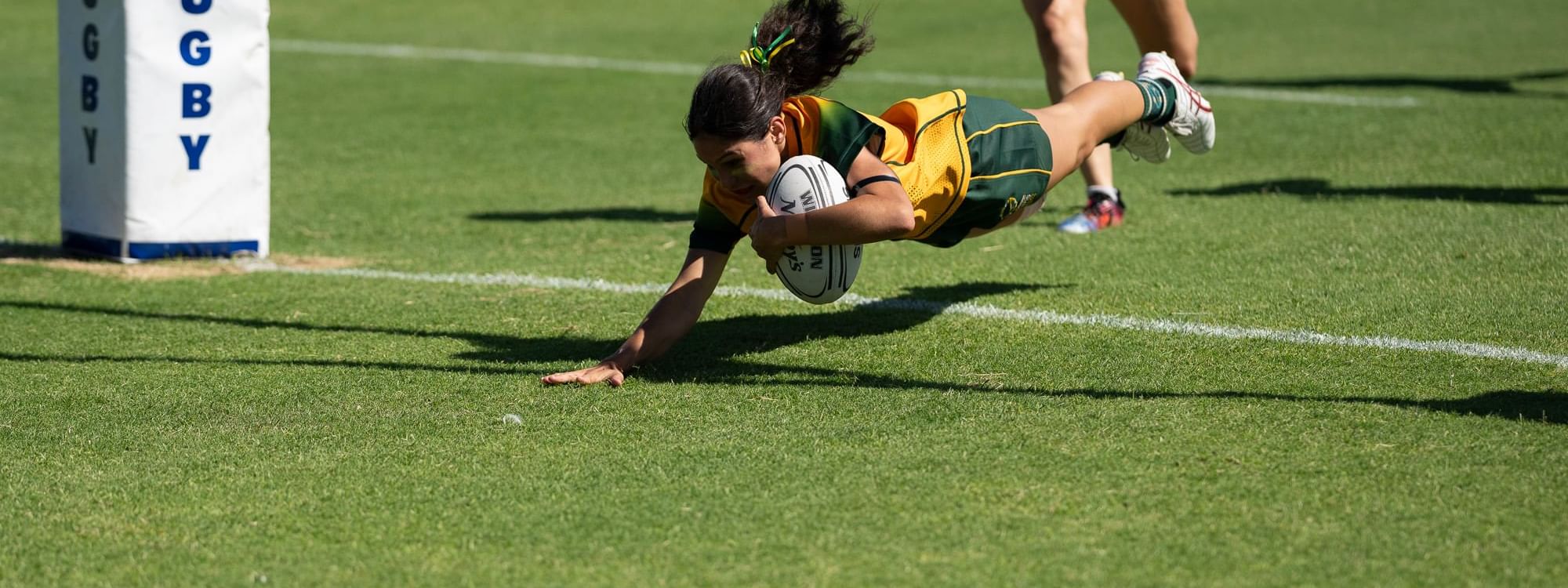 Rugby player diving to score with the ball as a teammate runs nearby on a sunny field at Novotel Sunshine Coast Resort