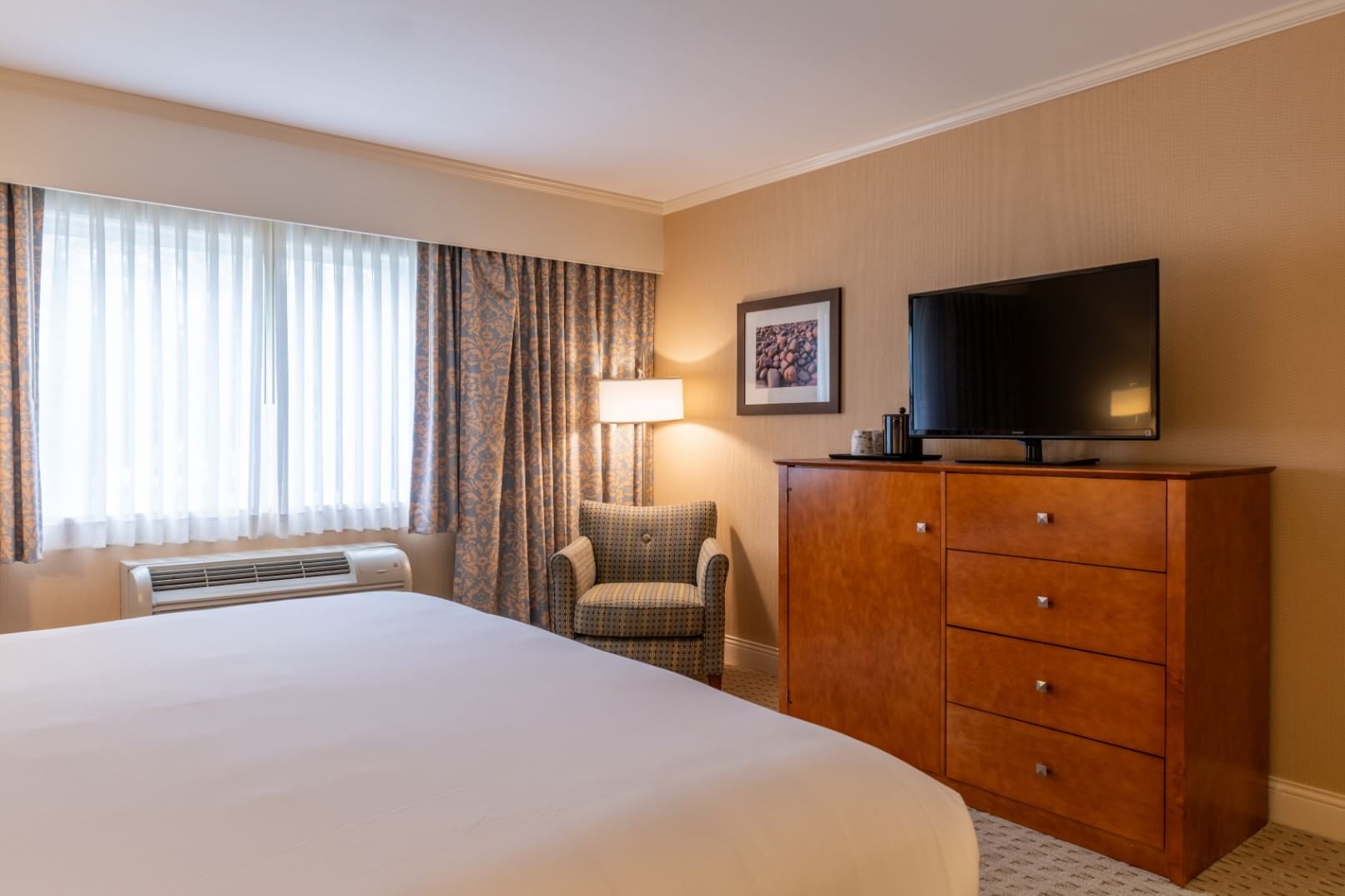 A hotel room with a bed, dresser, chair, and TV