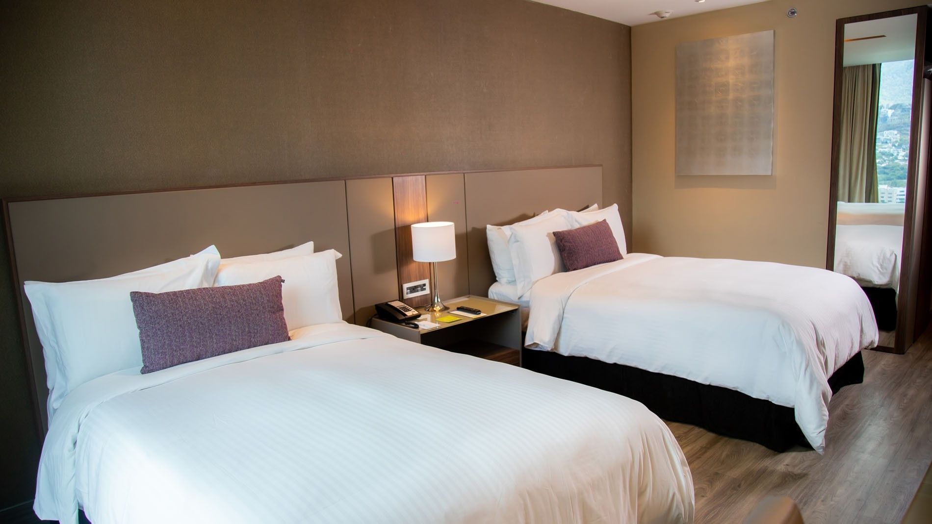 Deluxe Luxury King twin room with two white beds, warm lighting, and wooden floors at Camino Real Fashion Drive, Monterrey