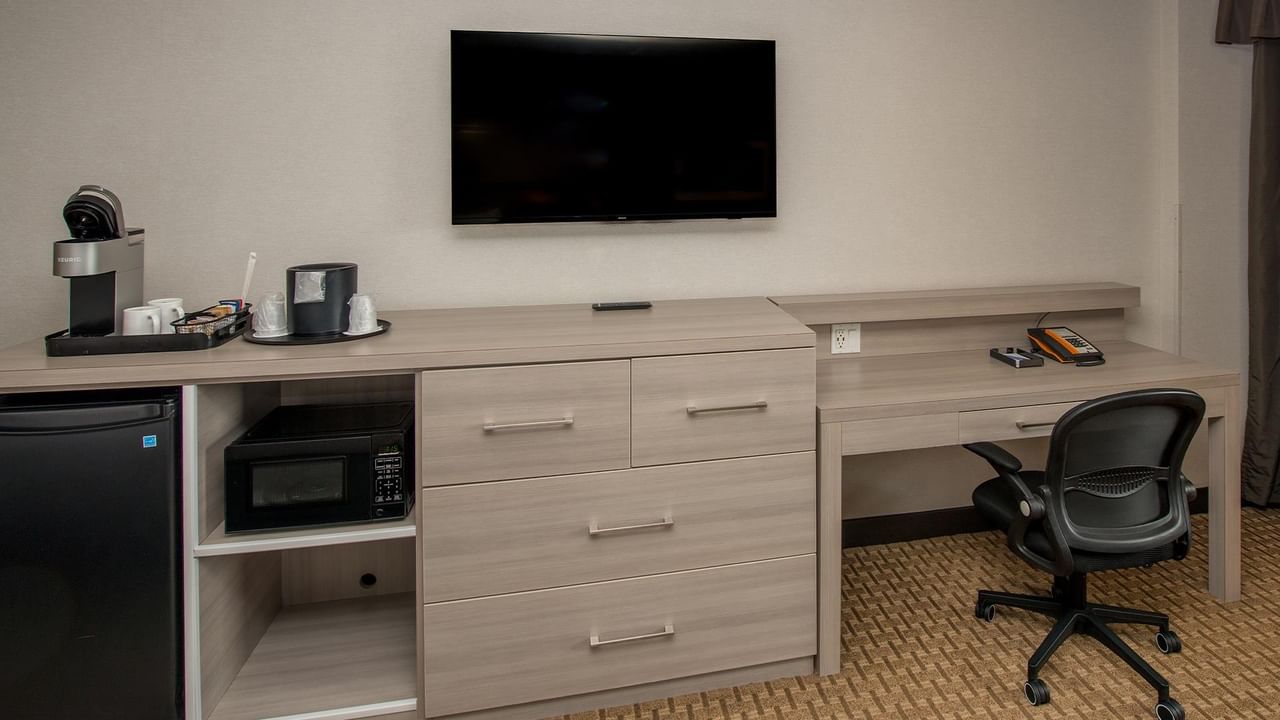 Modern guest room workspace with desk, ergonomic chair, flat-screen TV, and kitchenette at Coast Calgary University Area Hotel by APA.