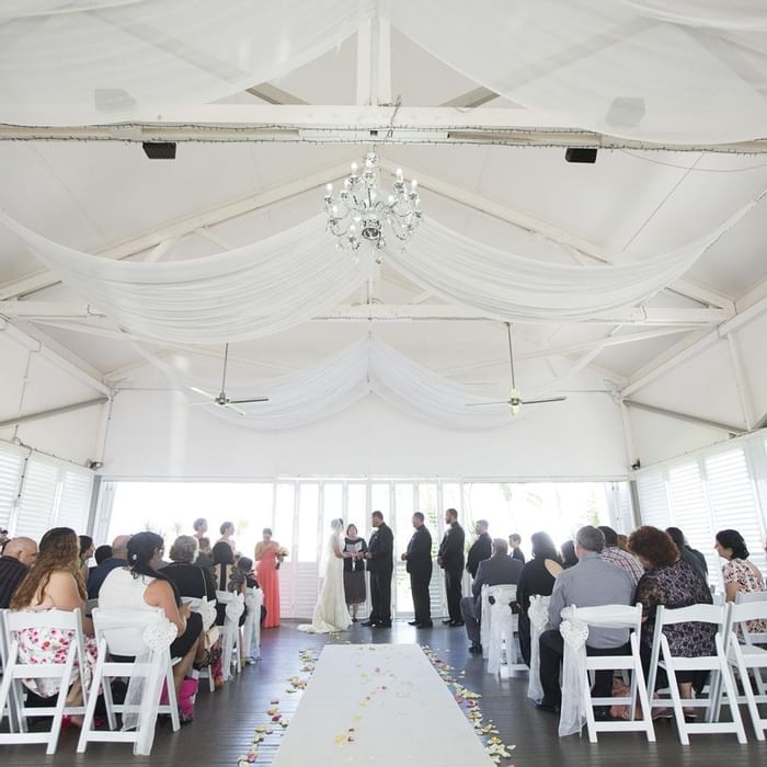 Wedding ceremony in a bright venue featuring guests seated on white chairs at Mercure Hotel Townsville