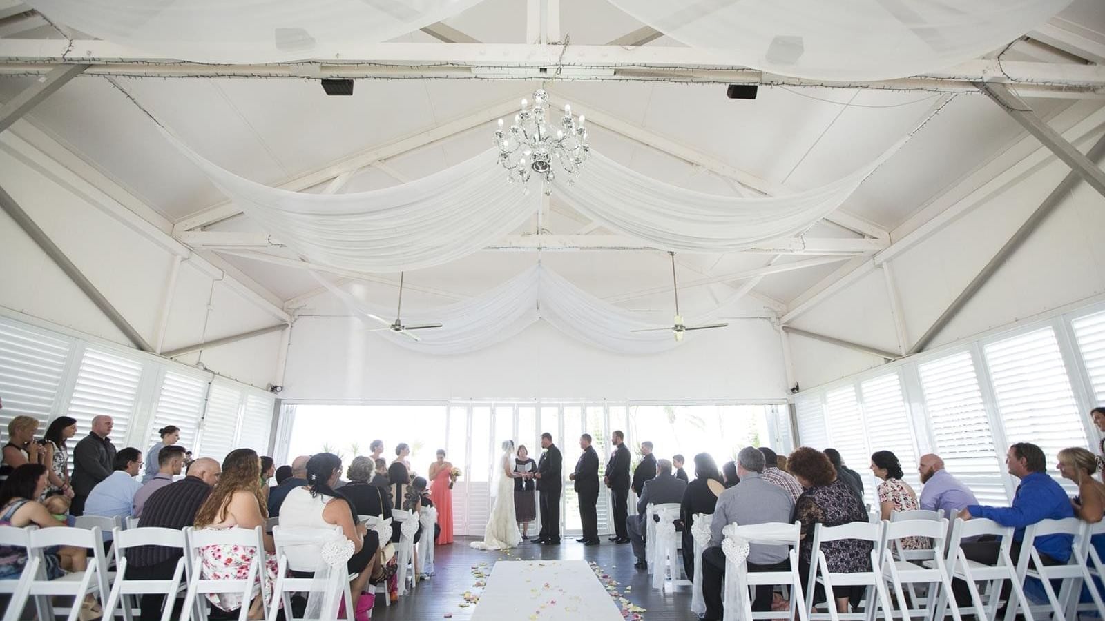 Wedding ceremony in a bright venue featuring guests seated on white chairs at Mercure Hotel Townsville