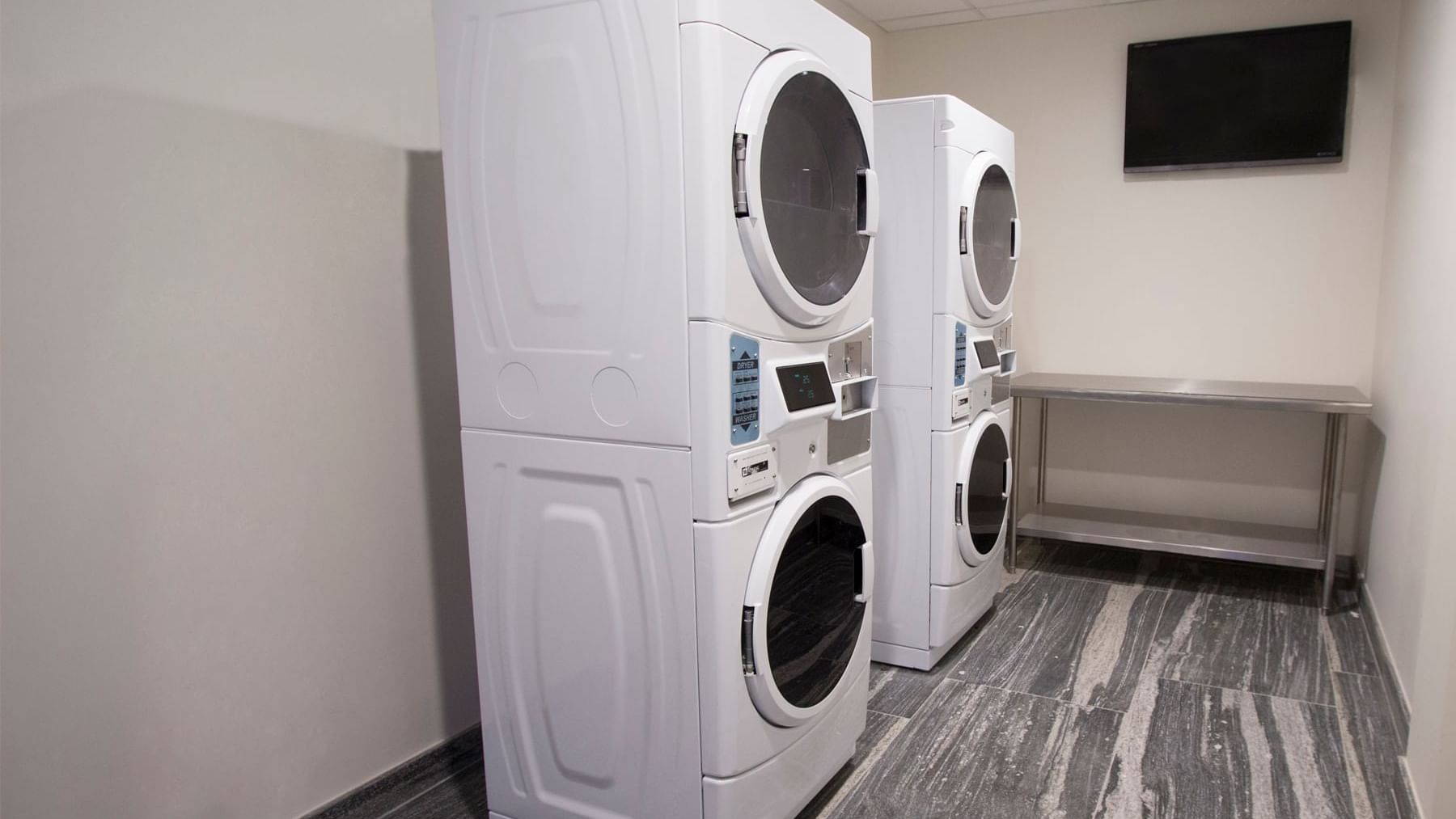 Laundry room features washer-dryer units, a folding table, and a TV at Fiesta Inn Suites Aeropuerto del Bajío