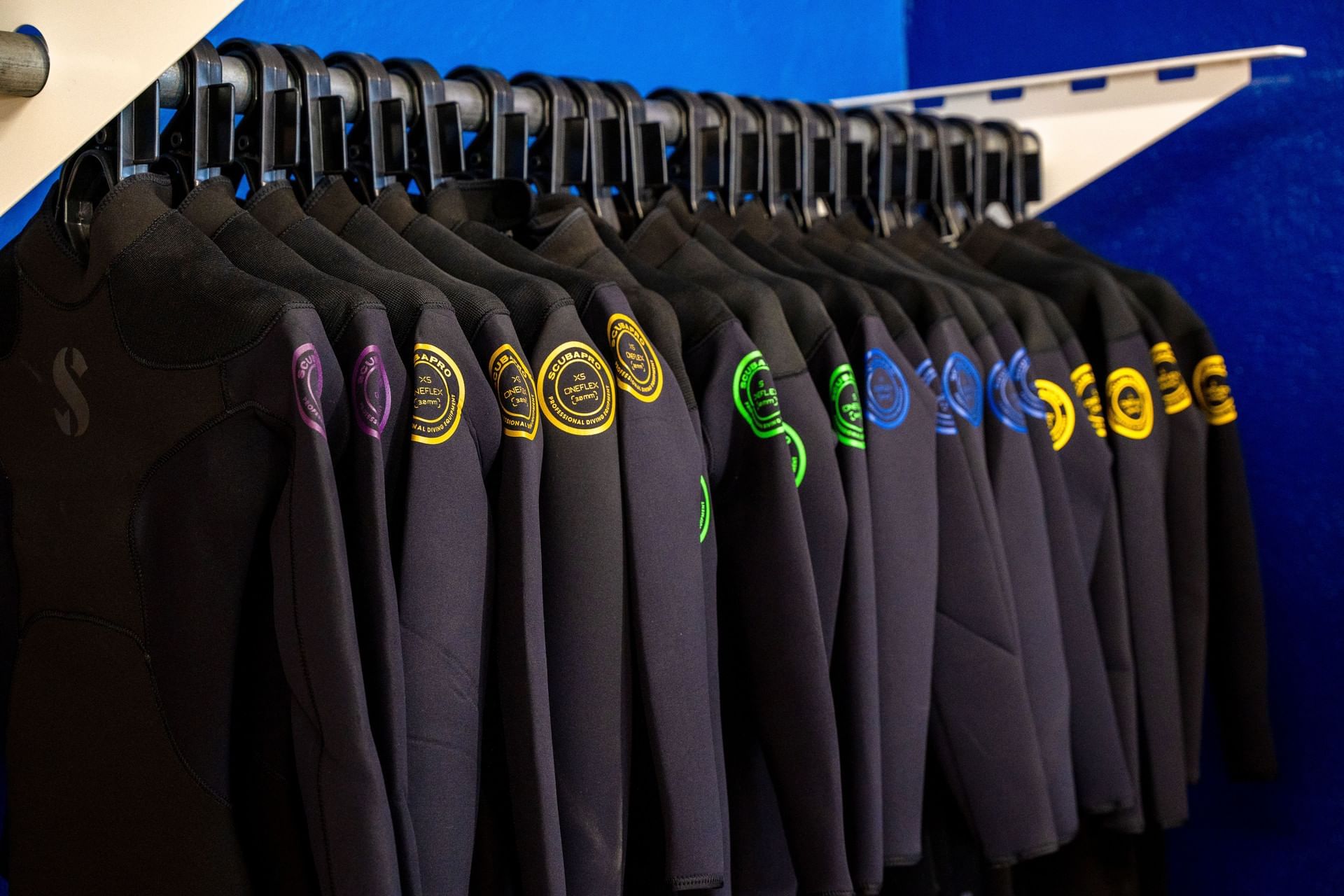 Neatly arranged Scubapro wetsuits with size badges hanging on a metal rack inside dive shop center at Golden Rock Resort