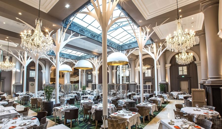 Dining table arrangements with chandeliers in La Verrière restaurant at Le Grand Hôtel des Thermes