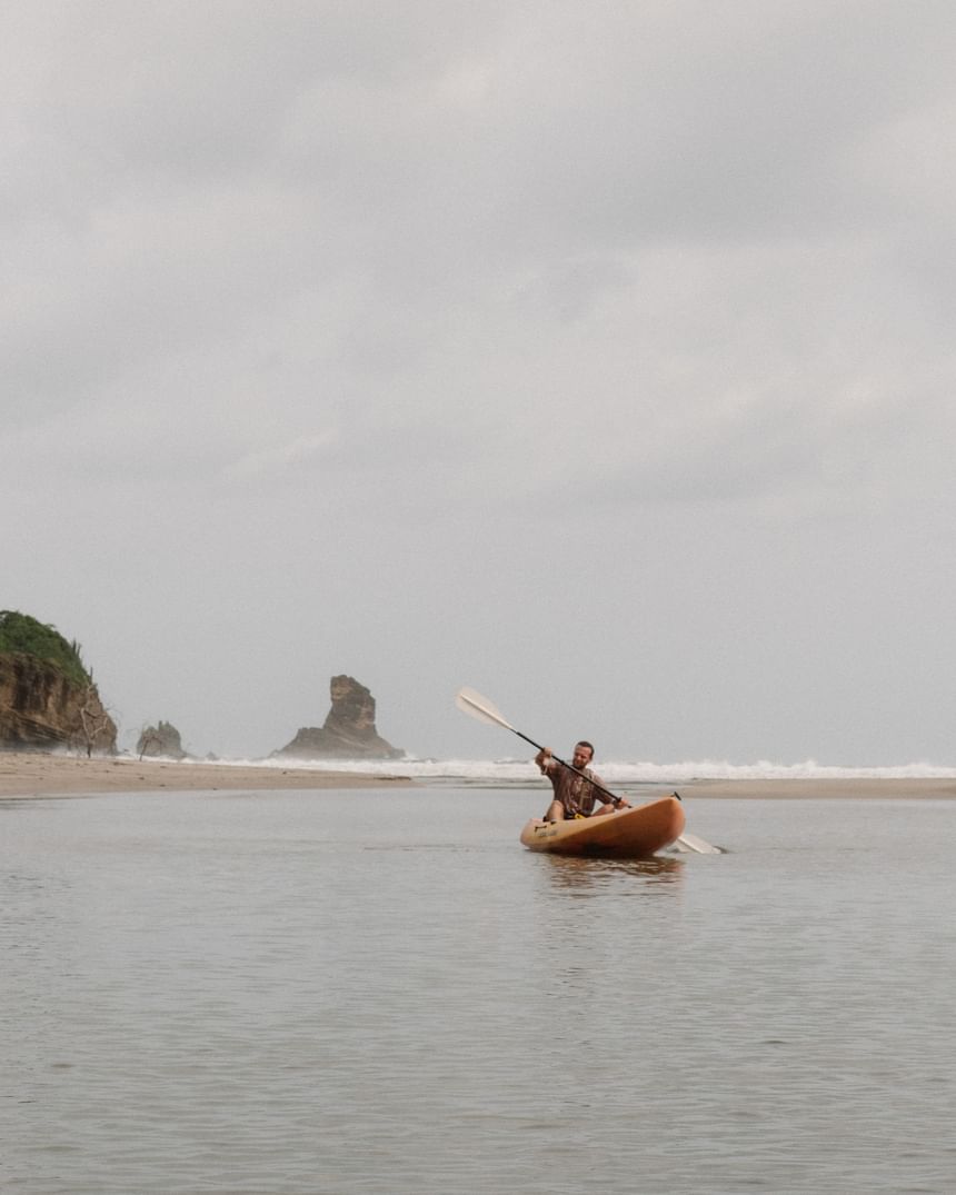 A man kayaking in calm estuary waters near the sand beach at Morgan’s Rock Reserve & Ecolodge