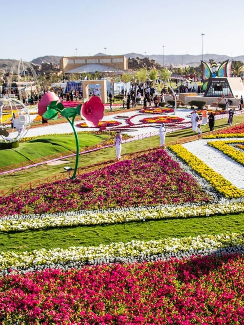 Des parterres de fleurs géométriques bordés de pelouses verdoyantes sous un ciel radieux, près d'un parc festif à l'hôtel Warwick Al Taif