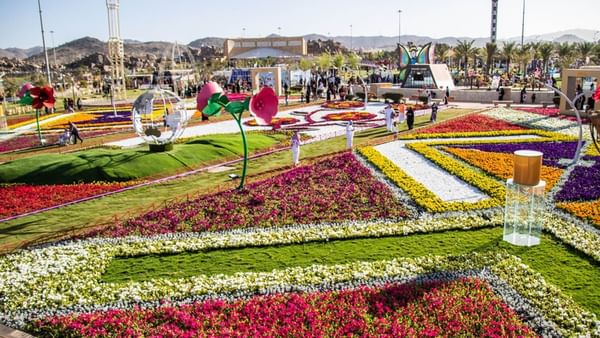 Des parterres de fleurs géométriques bordés de pelouses verdoyantes sous un ciel radieux, près d'un parc festif à l'hôtel Warwick Al Taif