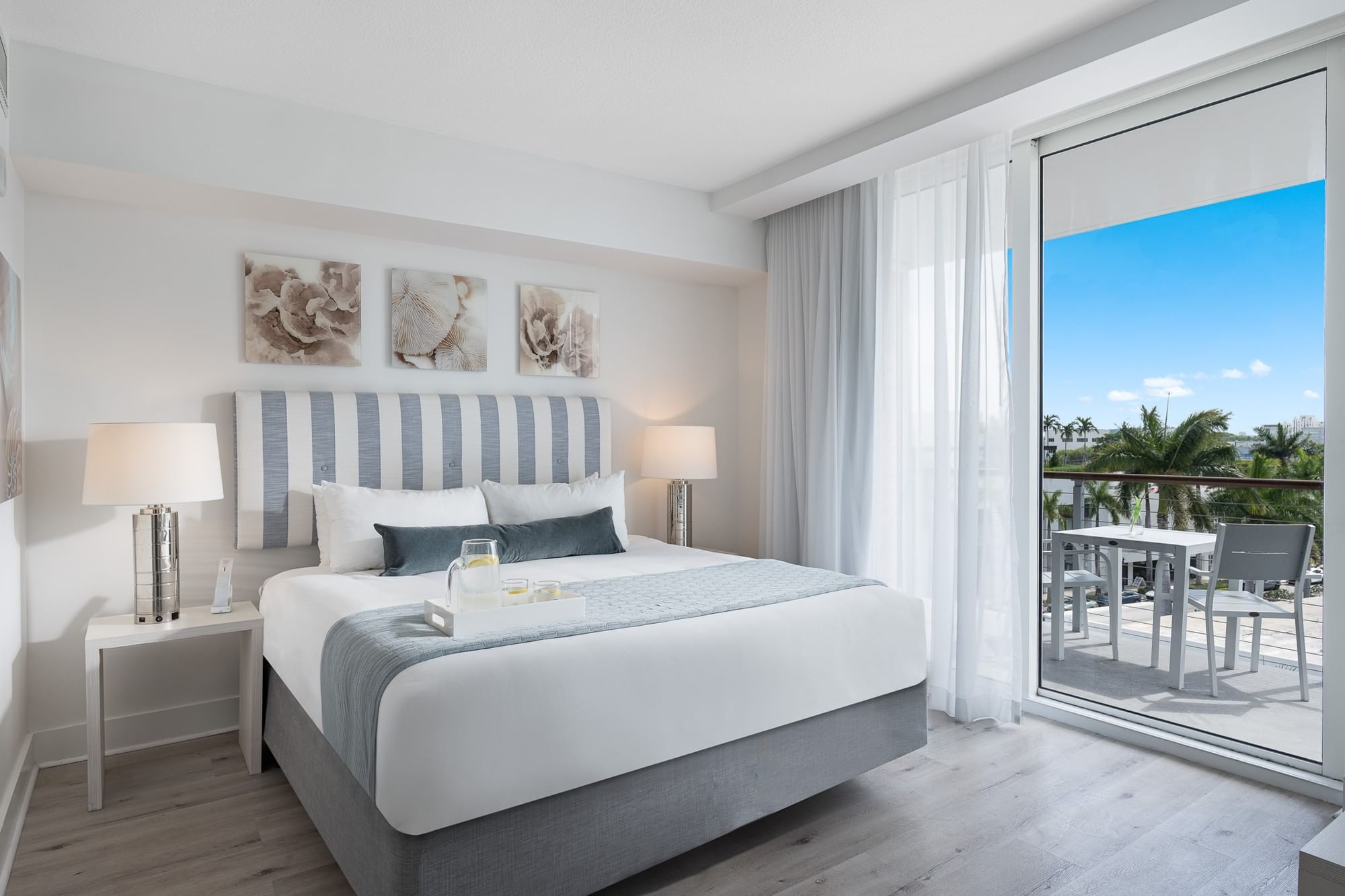 A wide view of a hotel room with a bed, nightstands, lamps, and a balcony with a view.