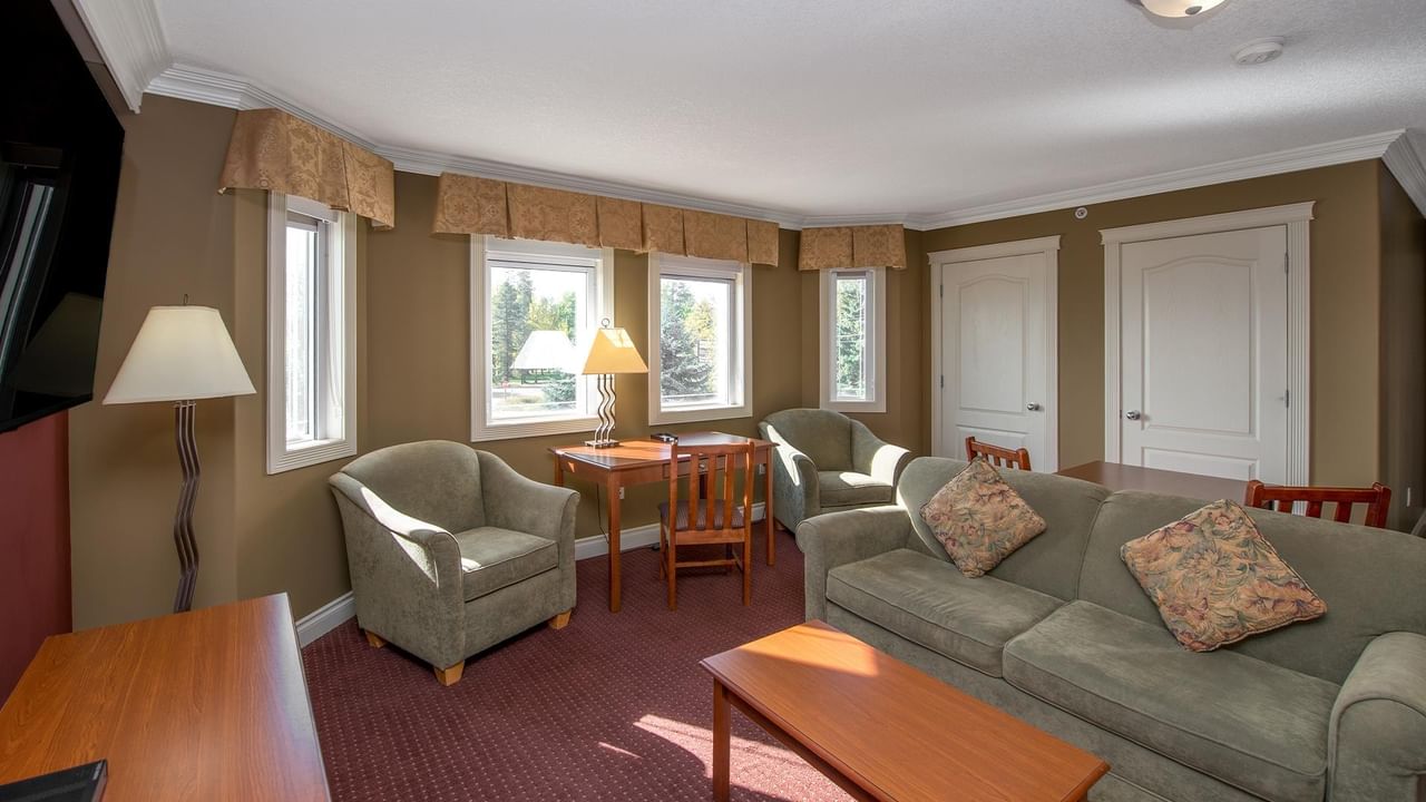 Bright suite with olive-green sofa, armchairs, wooden dining table, and multiple windows at Coast Edson Hotel.