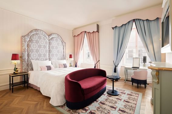 A room in hotel in Vienna with two big windows, a dressing table and a red velvet couch in front of a double bed