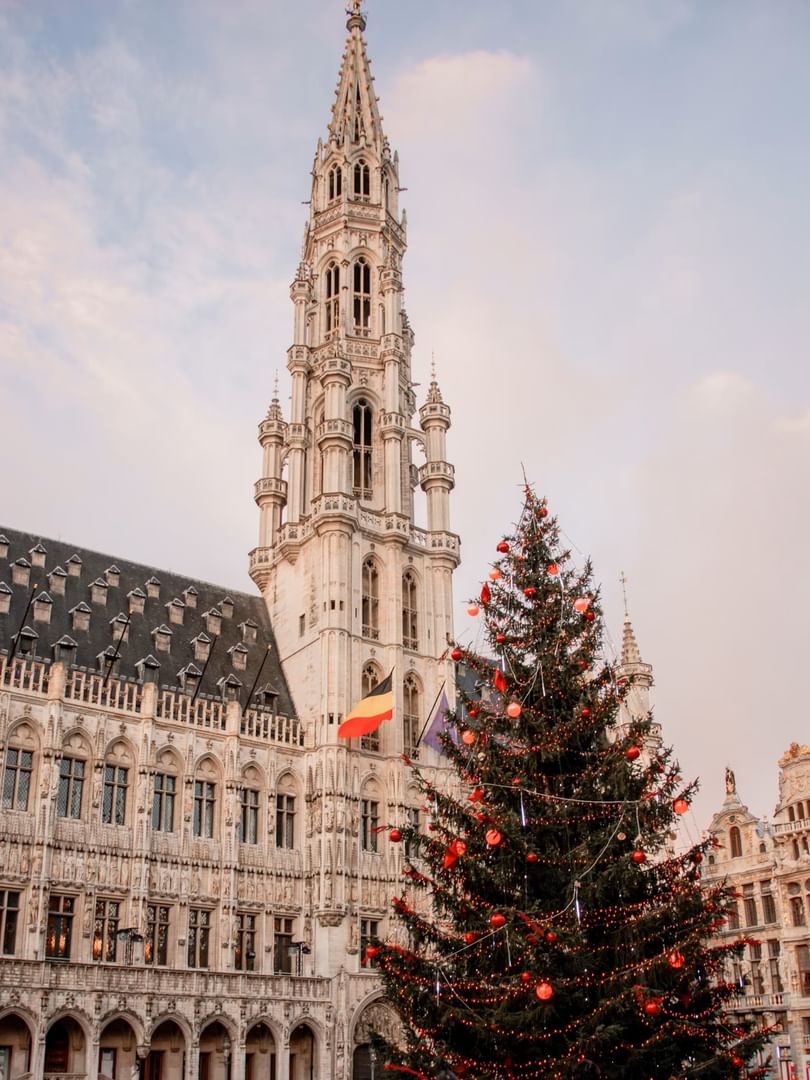 Decorated Christmas tree stands before ornate Gothic tower and historic buildings during Events in Brussels.