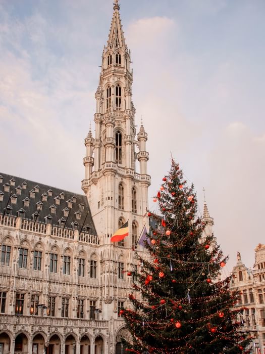 Decorated Christmas tree stands before ornate Gothic tower and historic buildings during Events in Brussels.