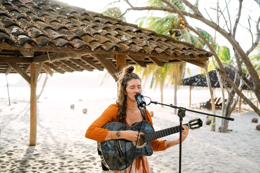 Woman playing guitar by a microphone under a wood roof at Morgan's Rock Reserve & Ecolodge