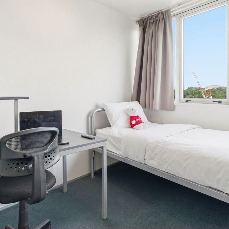 Neat room with bed, desk, chair, and window at Student Living Auckland Anzac.